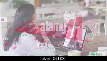 Image des icônes de médias sociaux contre la femme biraciale ayant un appel d'image sur ordinateur portable au bureau Banque D'Images