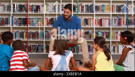 Frère masculin caucasien lisant à divers groupes d'enfants dans la bibliothèque de l'école Banque D'Images