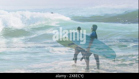 Couple diversifié tenant des planches de surf, marchant dans les vagues de l'océan Banque D'Images