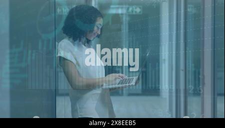 Une femme d'affaires biraciale heureuse travaille tard dans un bureau moderne, elle utilise un ordinateur portable whi Banque D'Images