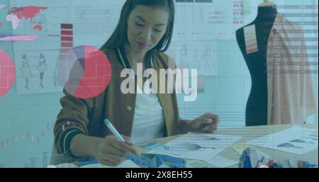 Image du traitement des données statistiques contre la créatrice de mode féminine biraciale travaillant en studio Banque D'Images