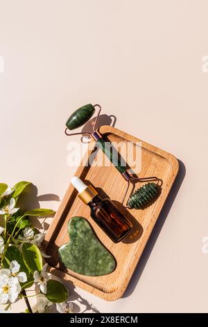 Roller Jade masseur, Gua Sha grattoir, huile de massage naturelle en bouteille avec compte-gouttes sur plateau en bois. La vue verticale de dessus. Soin spa. massage Banque D'Images