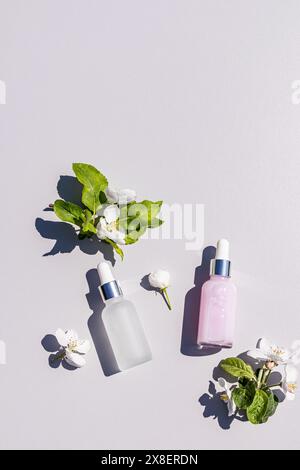 Deux bouteilles chics avec un produit cosmétique pour le soin des jeunes peaux sur un fond clair avec des brins de pommiers en fleurs. vue de dessus verticale Banque D'Images