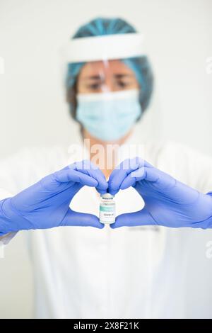 Portrait d'une travailleuse de soins de santé tenant un flacon de vaccin entre ses mains, formant une forme de coeur. Banque D'Images