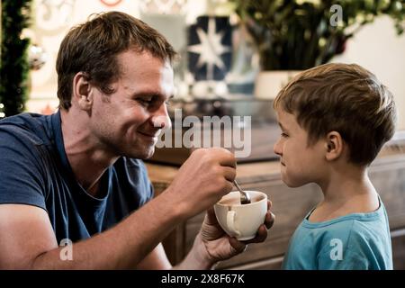 Père nourrit son fils avec une boisson au chocolat. Moments drôles de style de vie. Bonne éducation familiale de l'enfance. Banque D'Images