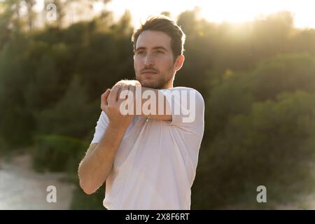 Portrait d'un homme souriant faisant des exercices dans la nature. Un homme qui s'étire à l'extérieur dans le parc pour l'énergie, la santé et le bien-être physique. Banque D'Images