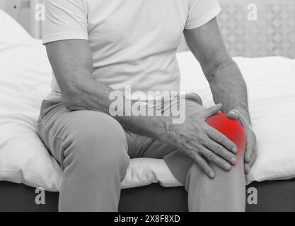 Homme souffrant de douleurs au genou sur le lit à la maison, gros plan. Effet noir et blanc Banque D'Images