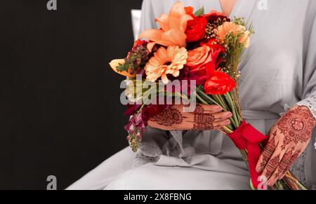 Mains, motif de henné et bouquet pour mariage en studio dans le respect de la tradition, de la foi et de la culture. Gros plan, mariage et femme pour walima ou nikah Banque D'Images