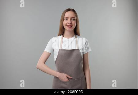 Belle jeune femme portant tablier de cuisine sur fond gris. Maquette pour le design Banque D'Images