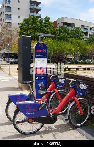 Viladecans, Barcelone, Espagne - 25 mai 2024 : une station de partage de vélos de ville avec des vélos bleus et rouges prêts à l'emploi. La toile de fond de l'appartement buildi Banque D'Images