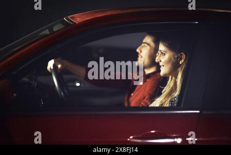 Couple, sourire et femme transport en voiture la nuit pour célébrer anniversaire, date ou voyage sur la route pour des vacances surprise. Heureux, les gens et l'homme conduisent Banque D'Images
