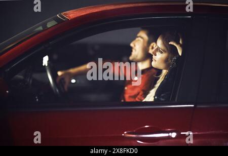 Femme, sourire et couple transport en voiture la nuit pour célébrer anniversaire, date ou voyage en voiture pour des vacances surprise. Heureux, les gens et l'homme conduisent Banque D'Images