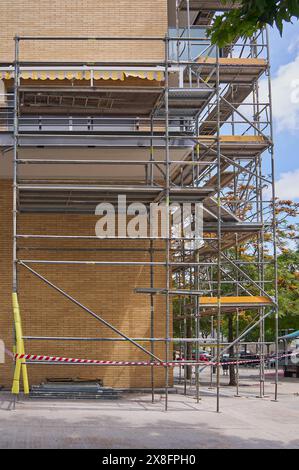 Échafaudages métalliques multi-niveaux contre le bâtiment avec isolation jaune sous ciel clair, indiquant des travaux en cours Banque D'Images