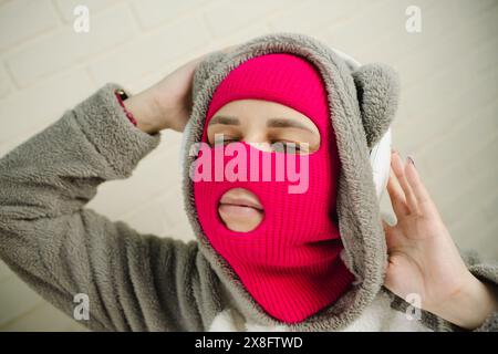 Femme en Balaclava rose dansant contre un mur de briques blanches Banque D'Images
