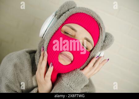 Femme en Balaclava rose dansant contre un mur de briques blanches Banque D'Images