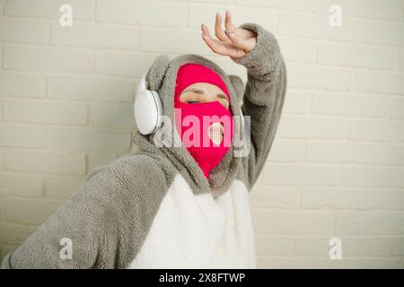 Femme en Balaclava rose dansant contre un mur de briques blanches Banque D'Images