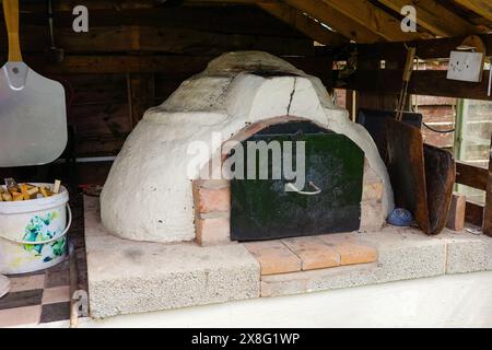 Four à pizza extérieur rustique dans un abri en bois, prêt pour la cuisson de pizzas maison avec une atmosphère chaleureuse et authentique. Banque D'Images