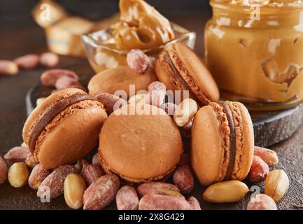 Un pot de beurre d'arachide, un aliment de base, est placé à côté des macarons et des cacahuètes sur la table. Ces ingrédients peuvent être utilisés dans diverses recettes de cuisine Banque D'Images