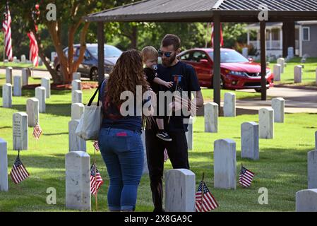 Raleigh, Caroline du Nord, États-Unis, 25 mai 2024; une jeune famille se joint à des bénévoles qui placent des drapeaux sur les pierres tombales de 6 000 au cimetière national de Raleigh avant le jour du souvenir. L'événement annuel, organisé par la Raleigh American Legion, honore les hommes et les femmes américains qui ont servi dans l'armée américaine en temps de paix et de guerre. Le cimetière national de Raleigh comprend les tombes des militaires de la guerre civile aux guerres d'Irak et d'Afghanistan. Credit d Guest Smith / Alamy Live News Banque D'Images