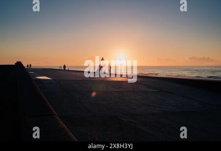 Une soirée paisible au bord de la mer avec des gens marchant sur la promenade, profitant du beau coucher de soleil sur l'horizon. Banque D'Images