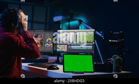 Tablette Chroma Key à côté de l'éditeur vidéo utilisant un logiciel de montage pour mettre à niveau les séquences. Dispositif d'écran isolé près du vidéaste freelancer finissant le projet dans l'appartement studio Banque D'Images