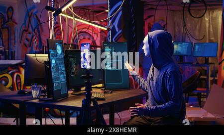 Des pirates informatiques dissimulant leur identité filmant une vidéo de rançon dans une base souterraine cachée, menaçant de divulguer publiquement des données volées si les demandes de paiement ne sont pas satisfaites, en utilisant le téléphone pour enregistrer des séquences de chantage Banque D'Images