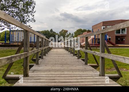 Pont en bois menant à l'aire de jeux et au bâtiment de l'école - entouré d'herbe verte et d'arbres sous un ciel nuageux. Prise à Toronto, Canada. Banque D'Images