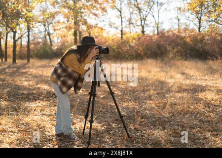 Belle femme caucasienne faisant une séance photo dans la forêt d'automne. Photographe professionnel photographiant un paysage par une journée ensoleillée à l'aide d'un appareil photo Banque D'Images