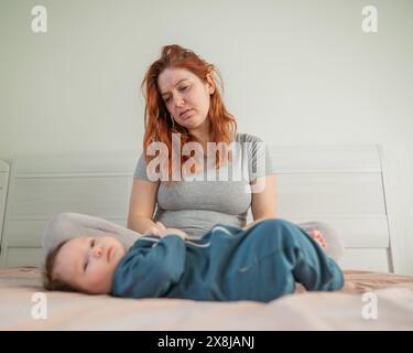 Femme avec dépression post-partum assise sur le lit à côté du nouveau-né. Banque D'Images