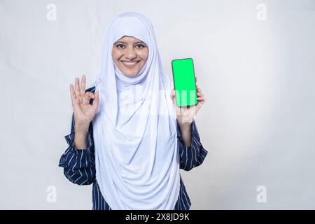 Portrait de femme musulmane indienne heureuse portant le hijab montrant un téléphone intelligent isolé sur fond blanc, technologie mobile, utilisateur d'Internet, médias sociaux Banque D'Images