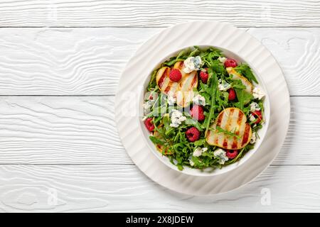 salade de poires grillées avec fromage bleu, salade de roquette et framboises fraîches mûres sur assiette blanche sur table en bois blanc, vue horizontale d'en haut, plat la Banque D'Images