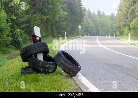 Le long d'une route de campagne, plusieurs vieux pneus jetés illégalement sont coincés sur un marqueur routier. Banque D'Images