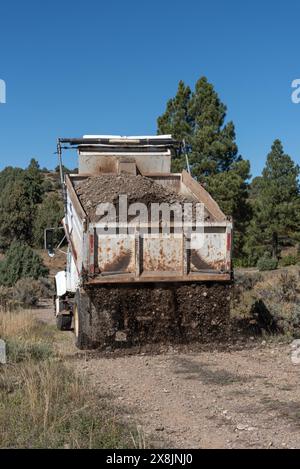 Vieux camion à benne blanche posant du gravier sur une route dans une partie reculée du nord du Nouveau-Mexique, États-Unis. Banque D'Images