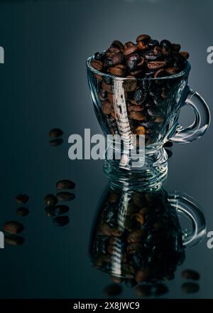 Grains de café de différents degrés de torréfaction dans une tasse de café transparente sur une table avec réflexion miroir Banque D'Images