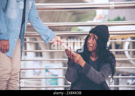 Femme aidant les mains aux sans-abri pauvreté mendiant homme tenant la main demandant l'argent travail et espérant de l'aide dans la ville sale impuissante assis dans les rues Banque D'Images