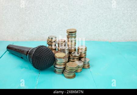 Microphone à côté de piles de pièces sur fond de tableaux bleus, concept de revenus de podcast Banque D'Images