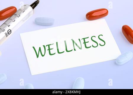 Wellness - concept de mot écrit sur la carte de visite à côté de pilules, vitamines et une seringue Banque D'Images