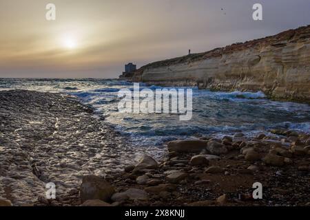 Le soleil se lève à l'horizon, illuminant un paysage de plage magnifique ; ses vagues paisibles de l'océan s'écrasent contre les falaises rocheuses du littoral. Banque D'Images