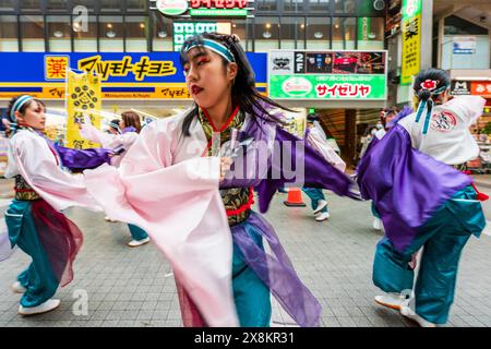 Gros plan d'une danseuse Yosakoi jouant dans une galerie marchande à Kumamoto, au Japon. Faisant partie d'un groupe de danseurs, elle tourbillonne dans un mouvement flou. Banque D'Images