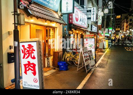 Vue le long de la rangée de restaurants et de dîners dans la soirée à Otsuka City, Tokyo. Le premier plan est un restaurant yakiniku (moyen grillé) avec des panneaux de menu à l'extérieur. Banque D'Images