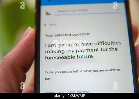 Main tenant un téléphone mobile affichant une page FAQ sur les difficultés de paiement futures, en se concentrant sur l'aide financière et les options de soutien. Banque D'Images