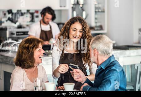 Belle barista féminine travaillant dans un café, servant les clients, couple âgé. Étudiant universitaire travaillant à temps partiel dans un café. Banque D'Images