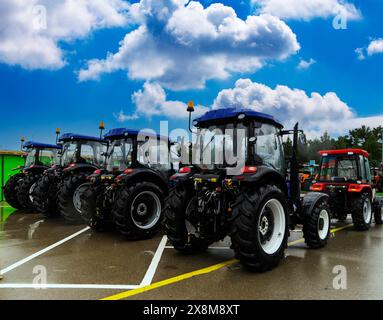 Les nouveaux tracteurs agricoles rouges de différents modèles se tiennent dans une rangée sur le site d'exposition en préparation pour le début des semis de printemps de l'agriculture, Banque D'Images