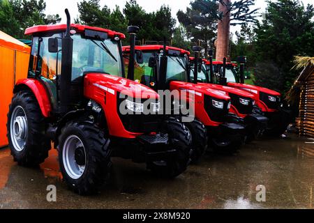 Les nouveaux tracteurs agricoles rouges de différents modèles se tiennent dans une rangée sur le site d'exposition en préparation pour le début des semis de printemps de l'agriculture, Banque D'Images