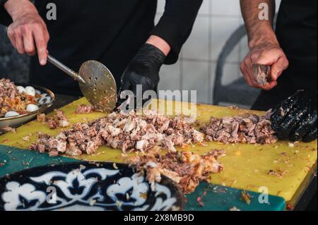 Les chefs masculins coupent la viande de bœuf bouillie avec des couteaux sur une planche à découper pour cuisiner le pilaf ouzbek oriental dans la cuisine d'un restaurant à Tachkent en Ouzbékistan Banque D'Images