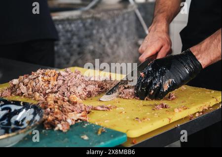 Chef masculin coupé la viande de bœuf bouillie avec un couteau sur une planche à découper pour cuisiner le pilaf ouzbek dans la cuisine d'un restaurant à Tachkent en Ouzbékistan Banque D'Images