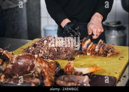 Homme chef couper la viande de bœuf bouillie avec un couteau sur une planche à découper dans la cuisine d'un restaurant à Tachkent en Ouzbékistan Banque D'Images