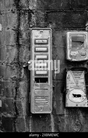 Une photo en gros plan en noir et blanc de vieux interphones rouillés et sonnettes sur un mur en béton altéré. Banque D'Images