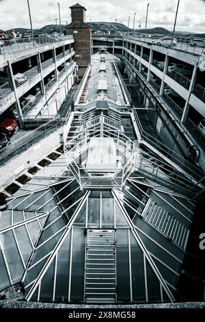 Architecture géométrique futuriste avec un toit en verre, situé le long d'un garage à plusieurs niveaux et d'un paysage urbain. Banque D'Images