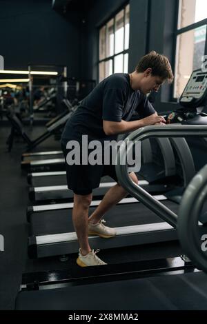 Plan vertical d'un coureur fatigué se reposant après un jogging sur un tapis roulant pendant une séance de cardio dans la salle de gym. Jeune homme satisfait debout sur le tapis roulant Banque D'Images